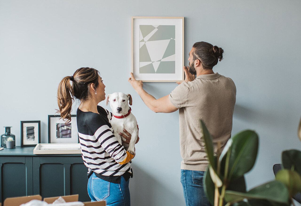 Man adjusting painting while woman and dog watch